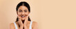 © Prostock-studio - Skincare Concept. Beautiful smiling young indian woman touching face and looking at camera, attractive eastern lady enjoying her flawless skin, standing over beige studio background, copy space