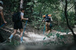 © qunica.com - Group of friends hiking through a forest path with backpacks and trekking poles. Outdoor adventure, exploration, and nature trail.