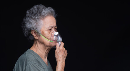 elderly woman wearing oxygen mask for breathing assistance on dark background.