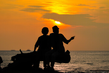 Two man talk each other sitting on the beach in silhouette. Boys enjoying sunset at the beach. Beautiful scenery at dawn, Twilight