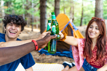 Diverse friendship toasting with beers at campsite, multicultural group enjoying outdoor picnic, social bonding in forest