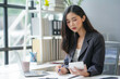 © amnaj - Focused young businesswoman in a modern office, using a calculator and jotting notes for a financial report. This image captures the essence of office life for a millennial entrepreneur