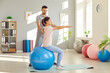 © Studio Romantic - Rehabilitation spine exercise on fitness ball, spinal therapy by male physical therapist in medical clinic gym room. Woman patient, med coach, nurse training back muscle, improving posture body health