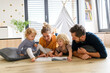 © Halfpoint - Young nuclear family playing with toys in a living room. Parents and children lying on floor, looking at children's story book, spending weekend day indoors.