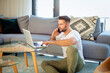 © sepy - Casual man sitting at home and using laptop and smartphone