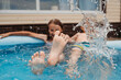 © Westend61 - Happy sibling splashing water in pool at back yard