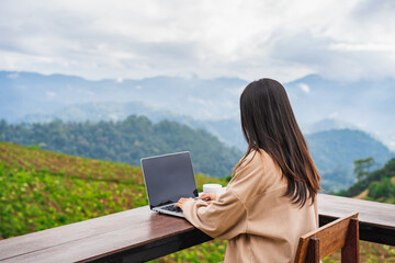 Young woman freelancer traveler working online using laptop and enjoying the beautiful nature landscape with mountain view