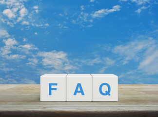 Poster - FAQ acronym on white block cubes on wooden table over blue sky with white clouds, Frequently asked questions, Business customer service and support concept