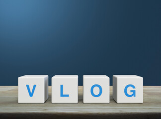 Poster - Vlog letter on white block cubes on wooden table over light blue wall, Vlog video marketing concept