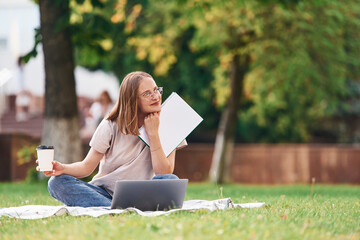 On the grass with laptop. Beautiful female student is outdoors near the university