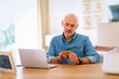 © gzorgz - Mid aged man sitting at desk and using notebook and holding a bank card in his hand