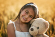 © peopleimages.com - Outdoor portrait, happy and girl with teddy bear for development, play and mockup in cornfield. Young child, smile and toy animal for bonding with healthy growth, space and calm weekend in nature