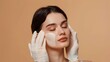 © LU - The beautician stroked the beautiful young woman's face with white gloves,  the lady's eyes closed on a beige background.    The concept of plastic surgery and facial skin care