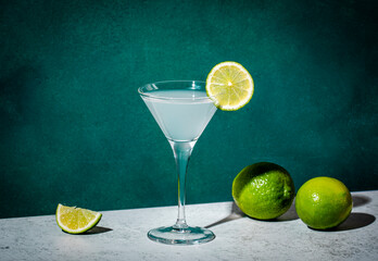 Wall Mural - Alcoholic cocktail with vodka, syrup, lime juice and ice in martini glass, dark green background