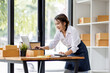 © David - SME concept. Young asian female ecommerce business owner prepares package box for customer and delivery check balance.  SME small business entrepreneur SME or freelance