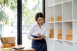 © David - SME concept. Young asian female ecommerce business owner prepares package box for customer and delivery check balance.  SME small business entrepreneur SME or freelance
