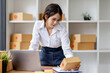 © David - SME concept. Young asian female ecommerce business owner prepares package box for customer and delivery check balance.  SME small business entrepreneur SME or freelance