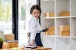 © David - Startup small business entrepreneur SME, asian woman checks stock on clipboard and parcels at home ,Success small business owner online sell marketing delivery, SME e-commerce telemarketing concept