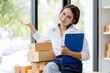 © David - Startup small business entrepreneur SME, asian woman checks stock on clipboard and parcels at home ,Success small business owner online sell marketing delivery, SME e-commerce telemarketing concept