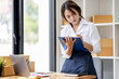 © David - Startup small business entrepreneur SME, asian woman checks stock on clipboard and parcels at home ,Success small business owner online sell marketing delivery, SME e-commerce telemarketing concept