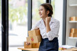 © David - Startup small business entrepreneur or freelance Asian woman using a laptop with box, Young success Asian woman with her hand lift up, online marketing packaging box and delivery, SME concept.