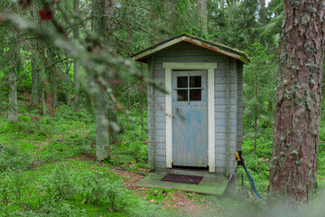 Wooden toilet in the green forest. Blue colored natural bio WC cabin among trees on green grass. Finland summer holidays