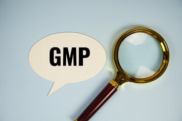 GMP text on speech bluble with magnifying glass top view on blue background