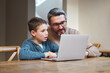 © CineLens2024/peopleimages.com - Laptop, learning and dad with child in home for online classes, school project and lesson. Family, education and father teaching boy on computer for help with studying, homework or student assignment