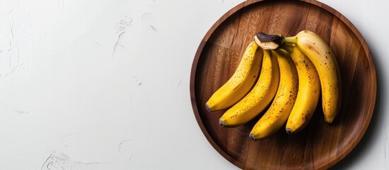 Leinwandbilder - Yellow bananas with copy space image on a wooden plate against a white background showcasing a nutritious tropical fruit from above