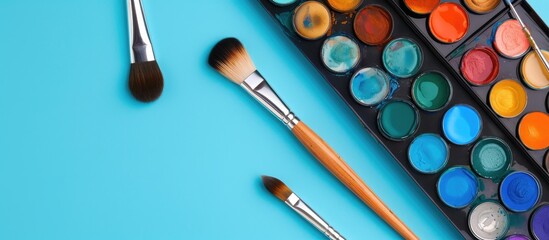 Poster - Close up of watercolor paints and brushes on a blue background with copy space image available
