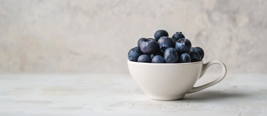 Poster - Side view of a white ceramic cup filled with fresh washed blueberries on a light grey backdrop offering ample copy space image