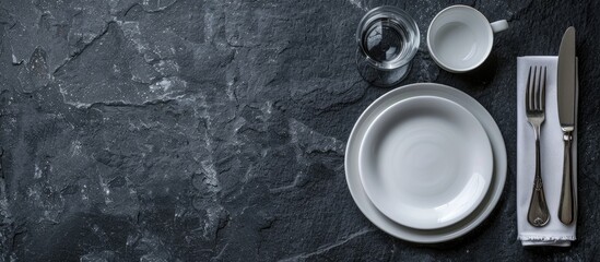 Poster - Top view of a set table with white crockery silverware and napkin on a dark stone surface offering a background for text or recipes with ample copy space image