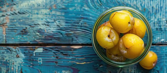 Poster - A top down view of organic yellow plums in a glass jar on a blue wooden surface perfect as a bio healthy food background with copy space image