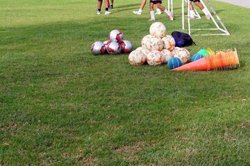 A lot of football and equipments on the grass with a group of people are playing soccer in a field.