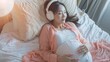© Sirichat. Camphol - Attractive Asian pregnant woman listening to music and lying in bed A pregnant woman uses headphones to play classical music for the baby in her womb. Learn