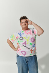 Young queer person in graffiti t-shirt poses confidently against white backdrop