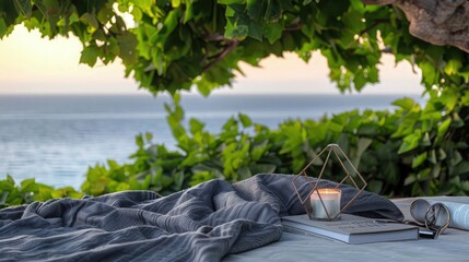 Wall Mural - An elegant grey blanket and a hardback poetry book with a modern geometric candle under a lush green tree. The distant sea merges with the evening sky.