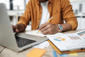 Poster - A man is focused on analyzing business strategy at his desk, using a laptop, charts, and paperwork. He is professionally working on data analysis with concentration in a modern office setting