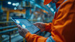 © khonkangrua - Industrial engineer in safety gear examining digital blueprints on a tablet in a factory environment.