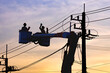 © Prapat - Silhouette of 2 lineman electricians on bucket boom truck are repairing electrical system on electric power pole against sunset sky background in evening time