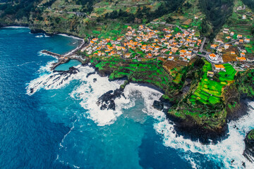 Aerial view of rough ocean with waves, volcanic beach and swiming pool in Seixal, Madeira, Portugal