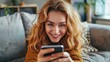 © Nijat - Sending happy messages. Lovely young lady lounging on the couch at home, grinning as she uses her smartphone
