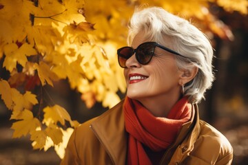 Sticker - Portrait of a tender woman in her 60s wearing a trendy sunglasses isolated in background of autumn leaves