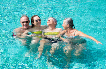 Wall Mural - Group of four cheerful friends having fun in outdoor swimming pool under the sun. Vacation and relax concept