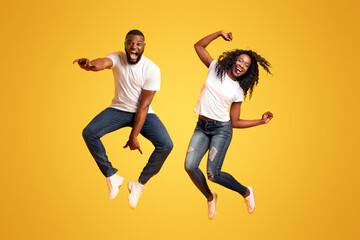 Wall Mural - Super Excited Black Couple Leaping On Yellow Studio Background, having fun together