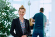 © .shock - Portrait of a Blonde Businesswoman in a Modern Office with Her Workspace and Colleagues in the Background.