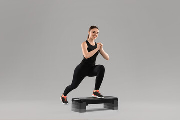 Wall Mural - Young woman doing aerobic exercise with step platform on light background