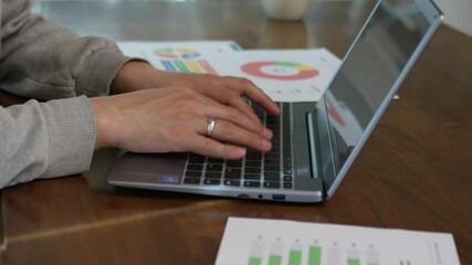 close up of man's hands typing on a laptop. documents on table in background