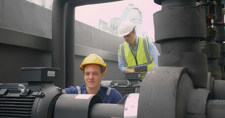 Wall Mural - Engineer man and worker looking inspecting maintenance insulated pipelines valve pump control on the roof at an industrial site. He is wearing a hard hat and safety vest