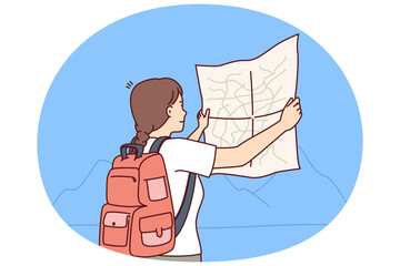 Wall Mural - Woman tourist looks at map choosing route for trip through wild during hike in mountainous area. Girl tourist with backpack behind back studies map of national park and enjoys journey